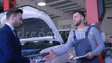 年轻的客户男子将汽车钥匙交给技术人员进行专业维修，并在服务车辆附近握手
